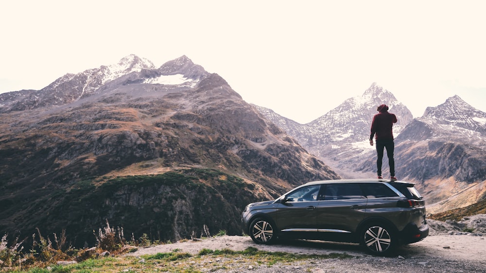 Hombre de pie en hatchback negro de 5 puertas a través de las montañas del glaciar marrón
