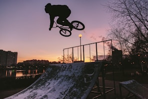 Sunset silhouette of Alexandre mid-air performing a BMX jump against a dark sky.