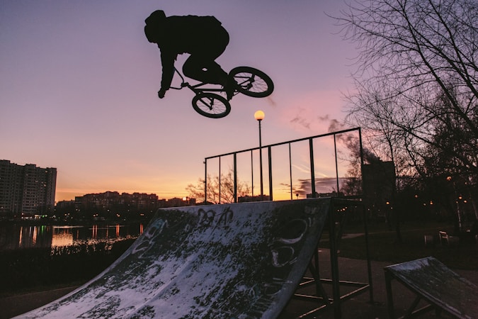 Silhouette of a BMX rider performing a trick against a bright sky at an outdoor demonstration