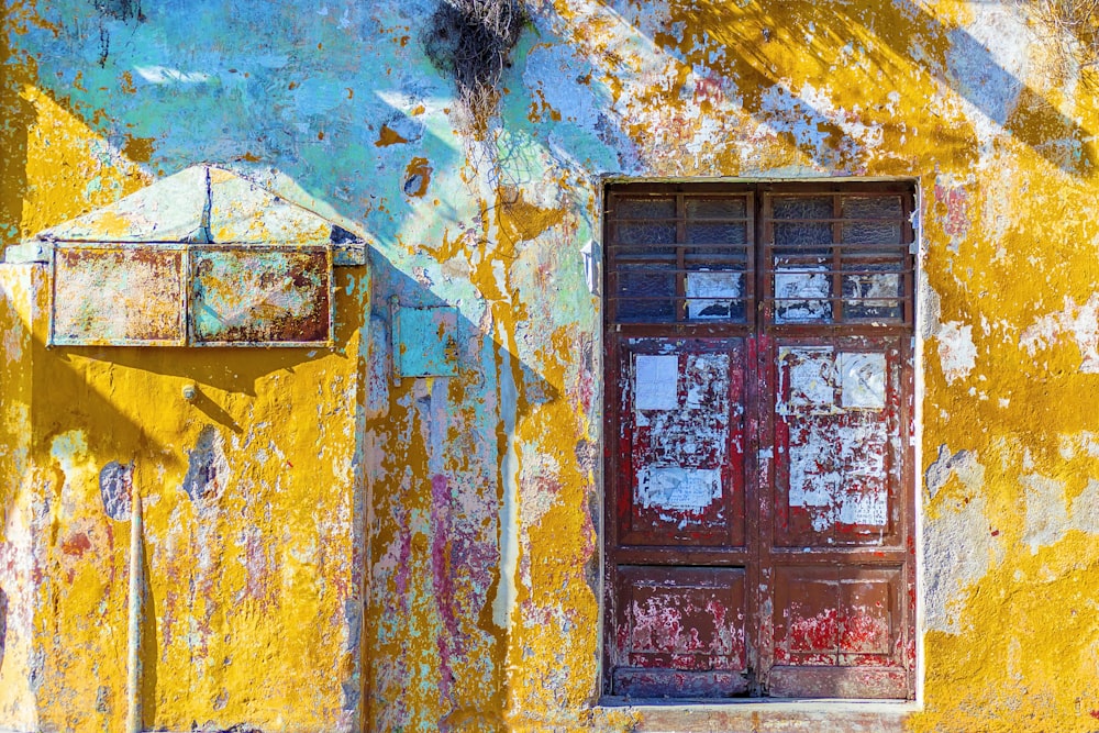 Pared de hormigón pintado de amarillo, blanco y verde azulado con ventana de madera roja de 2 puertas