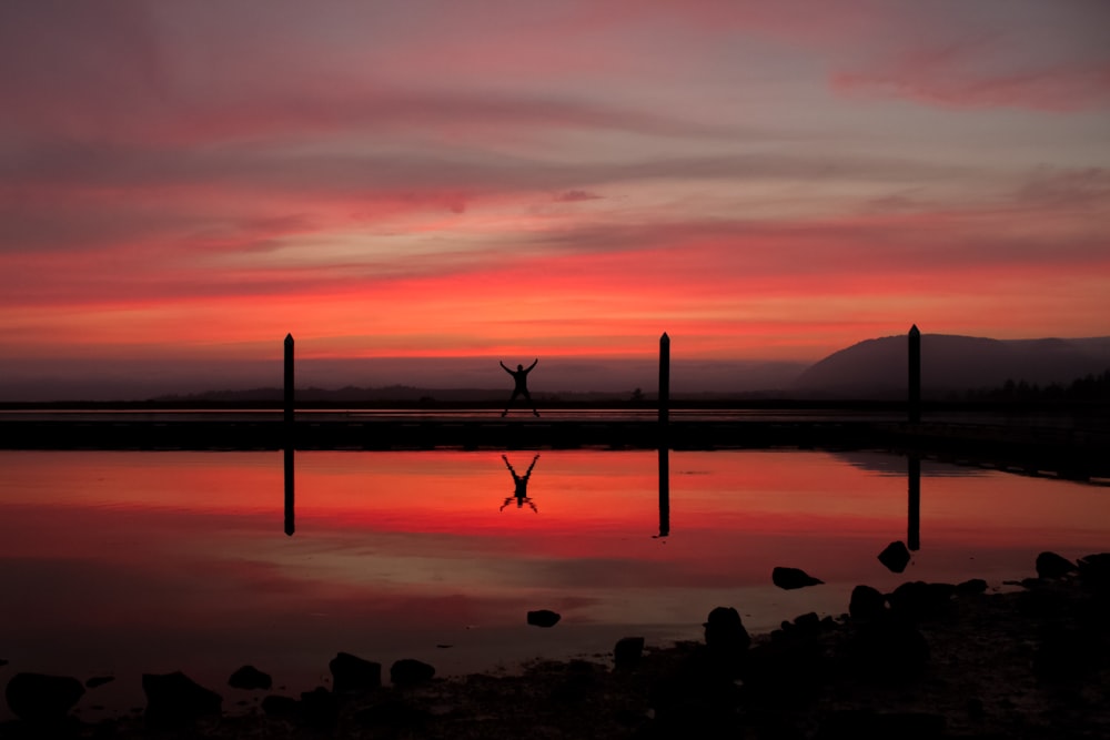 silhouette of person standing beside body of water during golden hour