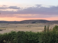 An expansive landscape with rolling hills under a soft, pastel sunset sky.