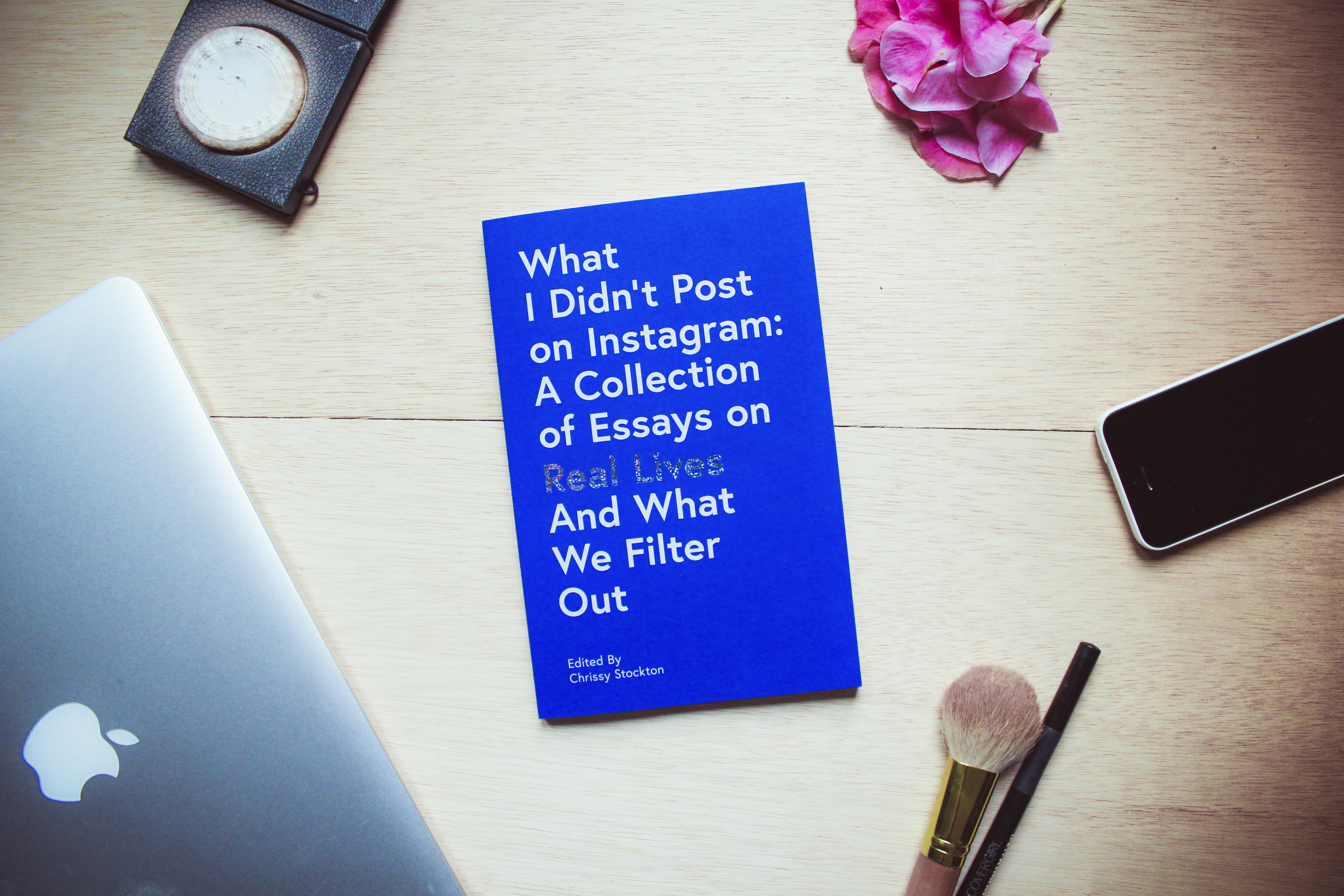 A table or desktop setting of the book, “What I Didn’t Post on Instagram” surrounded by objects one might use to prepare for a selfie (makeup, iPhone, laptop). We asked women to share the truth behind their Instagram photos for a collection of essays. The book ‘What I Didn’t Post On Instagram’ by Chrissy Stockton exposes that we are all a little confused when it comes to life. We are all just trying to belong. The essays housed in this collection are deeply honest, real, and make you feel seen and connected as they reveal the humanness within a platform that has quickly become less than human.