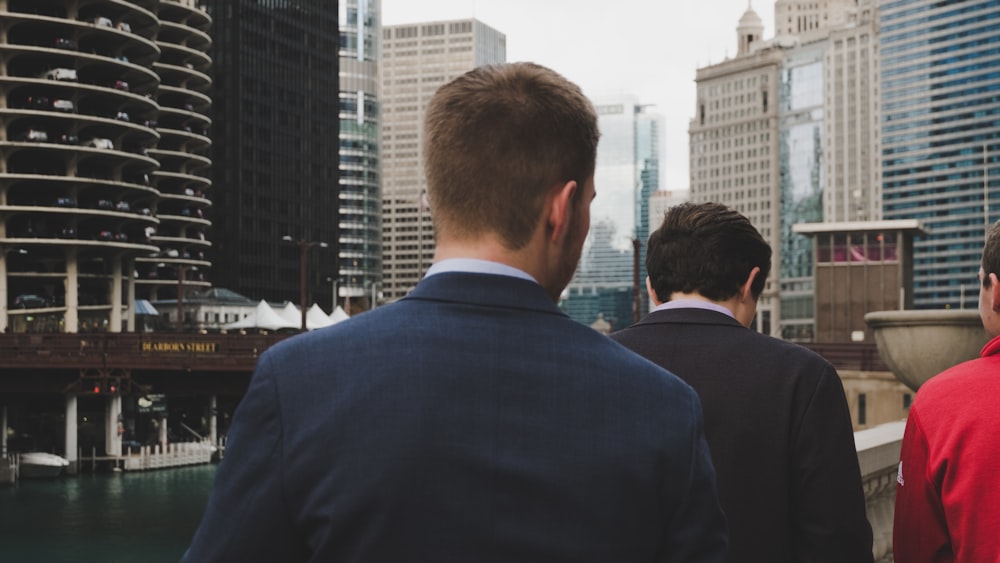 man wearing blue blazer standing behind two men during daaytime