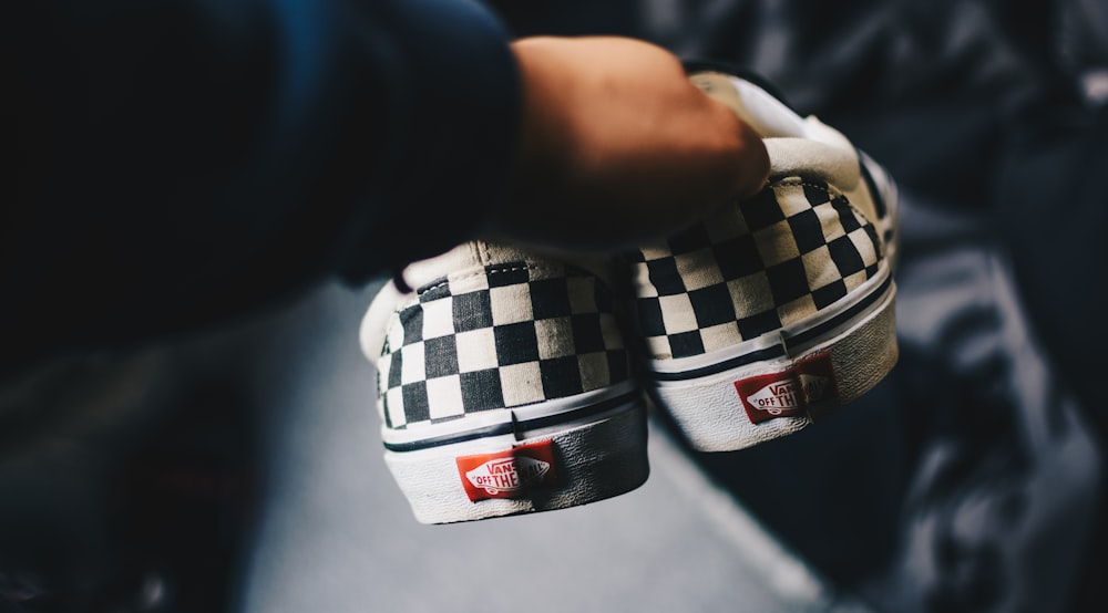 persona sosteniendo un par de Vans Era a cuadros en blanco y negro fotografía de primer plano