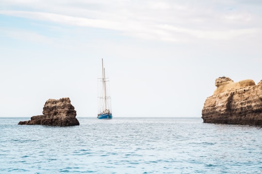 blue boat between brown rock formation under blue and white sky at daytime in Vilamoura Portugal