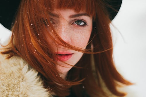 Woman with red hair wearing black hat in snow in article for winter hair care
