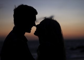 silhouette of man and woman about to kiss on beach during sunset