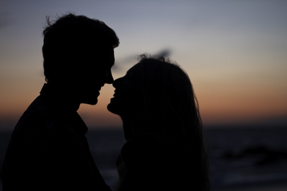 silhouette of man and woman about to kiss on beach during sunset