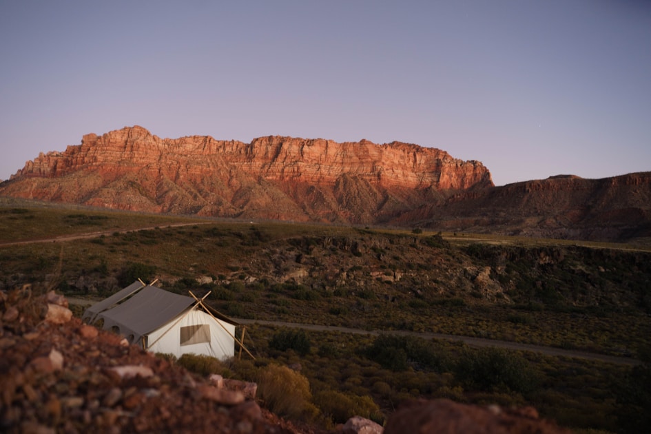 Canvas wall tent hunting camp pitched below red sandstone cliffs at dusk