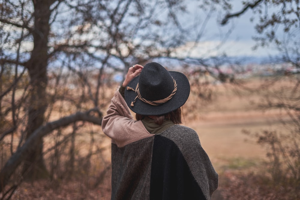 mulher que usa o chapéu preto em pé perto das árvores verdes