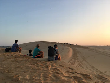 Group of travelers enjoying a sunset in the Moroccan desert with a 4x4 vehicle nearby.