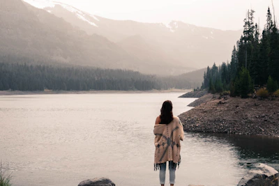 A serene lakeside at dawn with women meditating quietly, wrapped in cozy shawls.