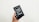 A hand is holding a box containing an older model of a smartphone with a black front and visible app icons. The box is black and features an image of the phone on the front.