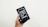 A hand is holding a box containing an older model of a smartphone with a black front and visible app icons. The box is black and features an image of the phone on the front.