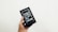 A hand is holding a box containing an older model of a smartphone with a black front and visible app icons. The box is black and features an image of the phone on the front.