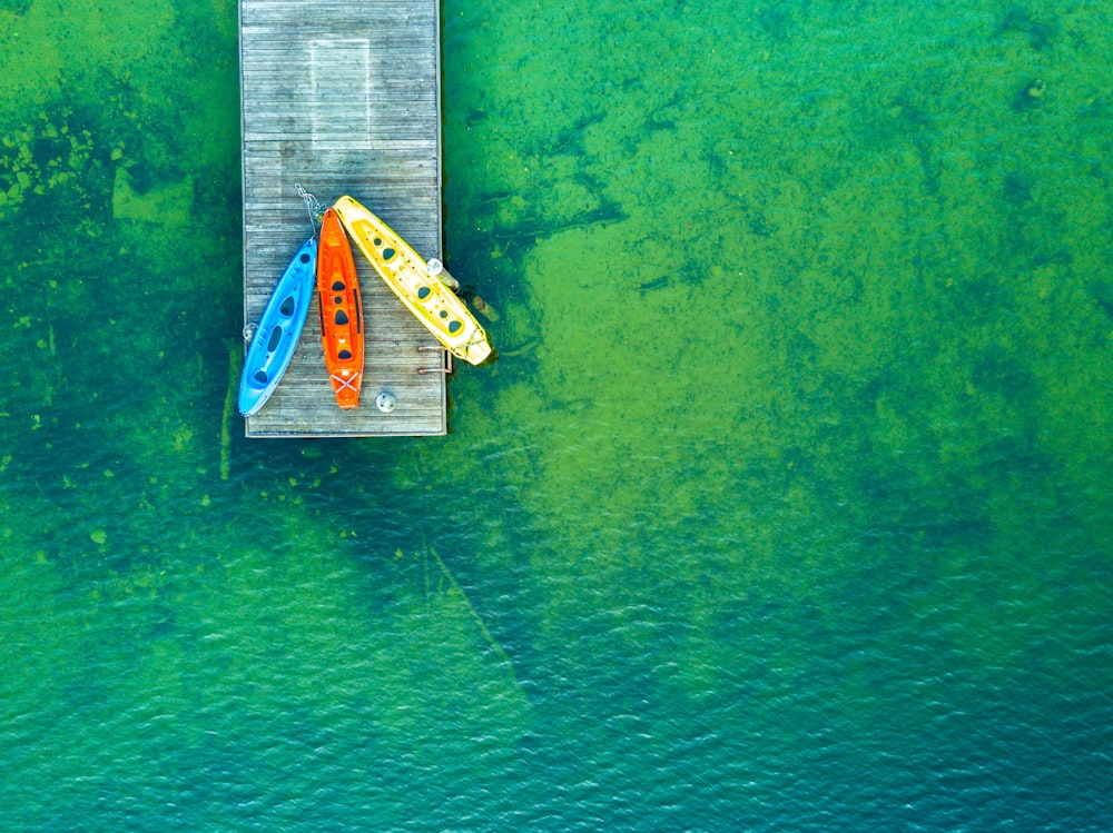 Fotografia a volo d'uccello di kayak rossi, blu e gialli su un molo di legno vicino a uno specchio d'acqua