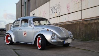 silver Volkswagen Beetle near white and brown wall during daytime