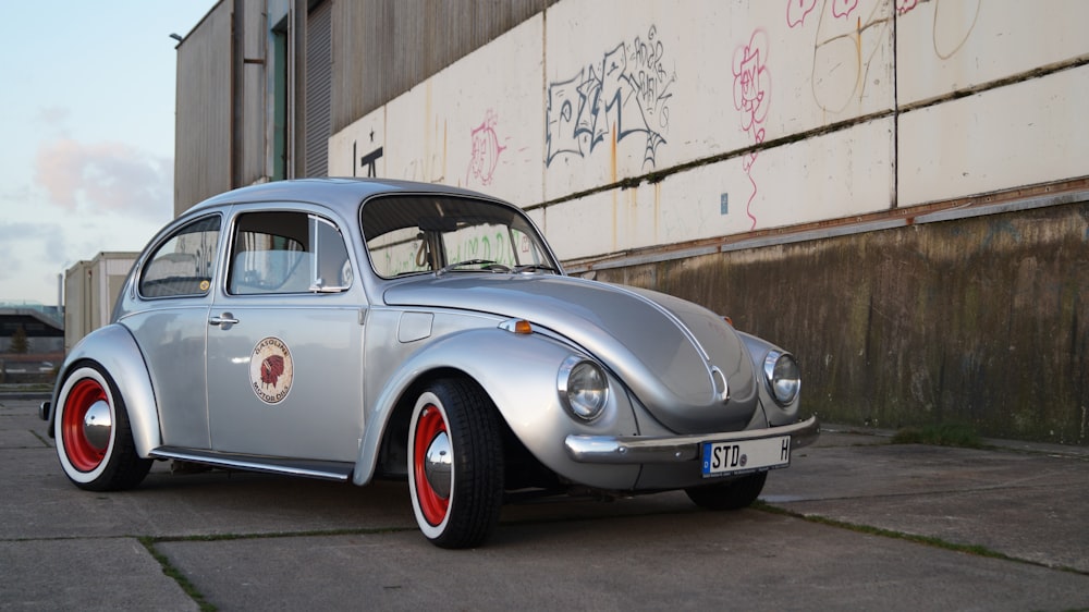 silver Volkswagen Beetle near white and brown wall during daytime