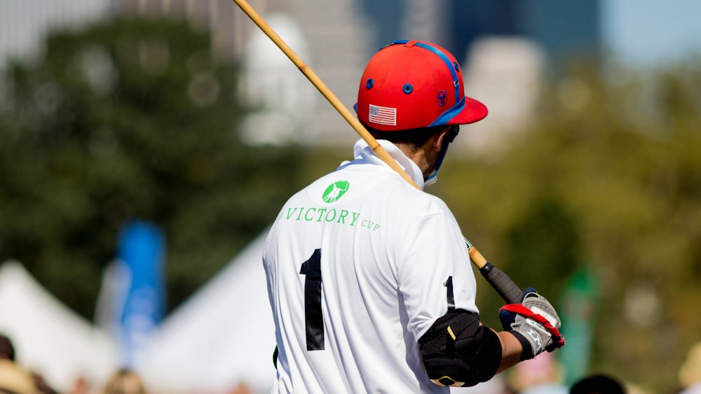 man wearing white and black 1 jersey shirt holding brown and black stick