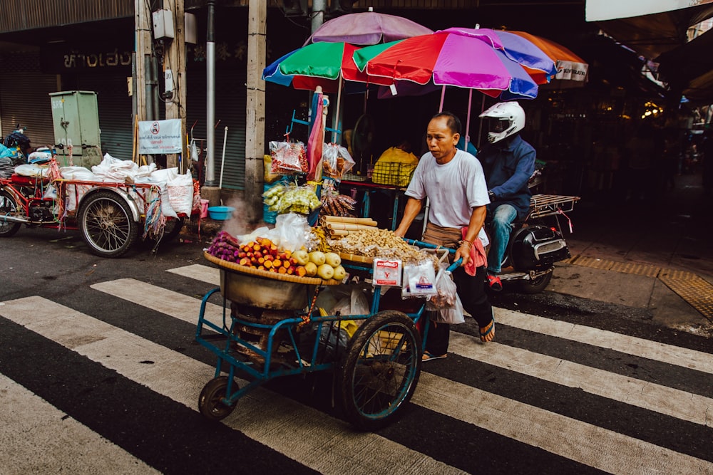 man pushing his food cart on pedestrian lane during daytime