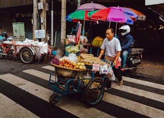 man pushing his food cart on pedestrian lane during daytime