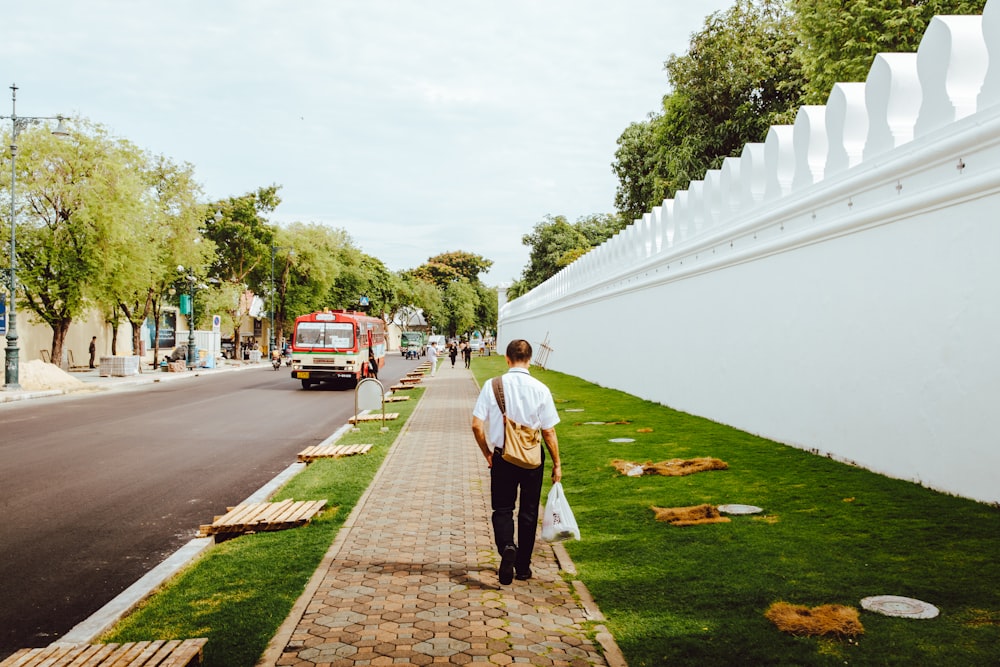 Persona caminando sobre el camino de ladrillos de arcilla marrón cerca de la pared de concreto blanco