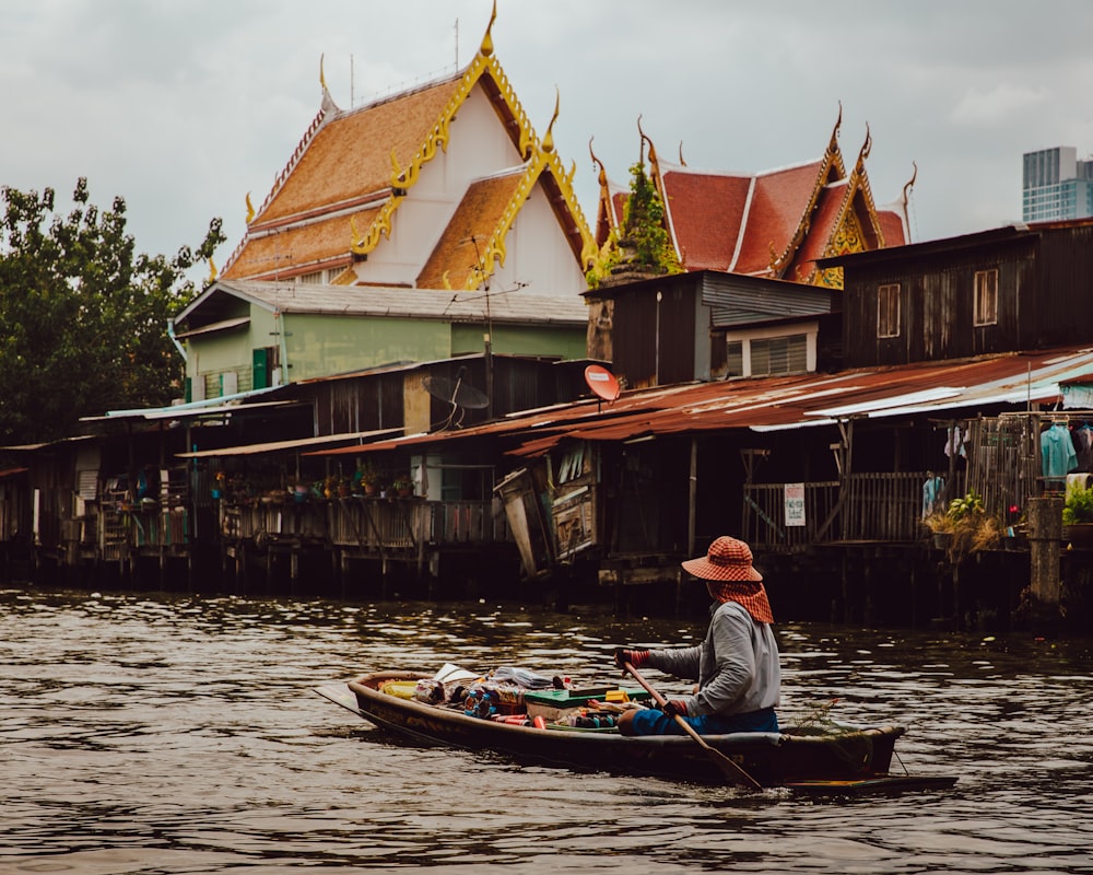 woman riding boat holding paddle on calm body of water in front of houses