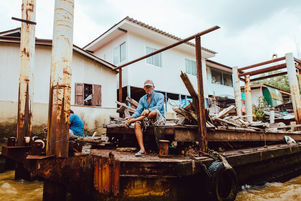 man wearing blue shirt sitting near brown metal while fishing during daytime