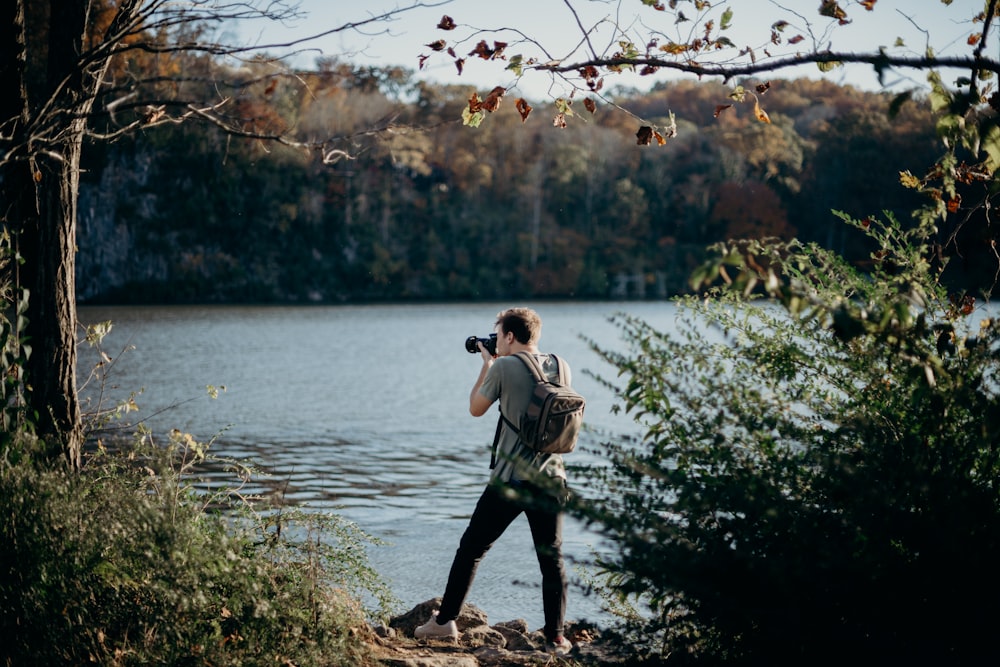 homem com mochila tirando foto ao lado do lago