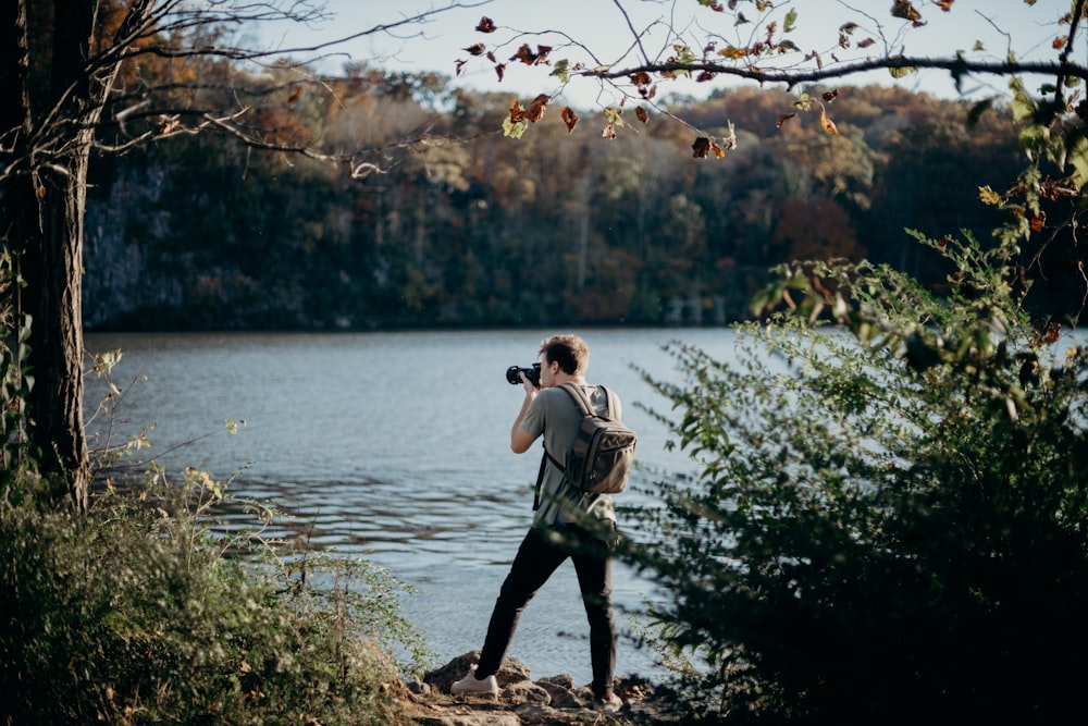 uomo con zaino che scatta foto accanto al lago