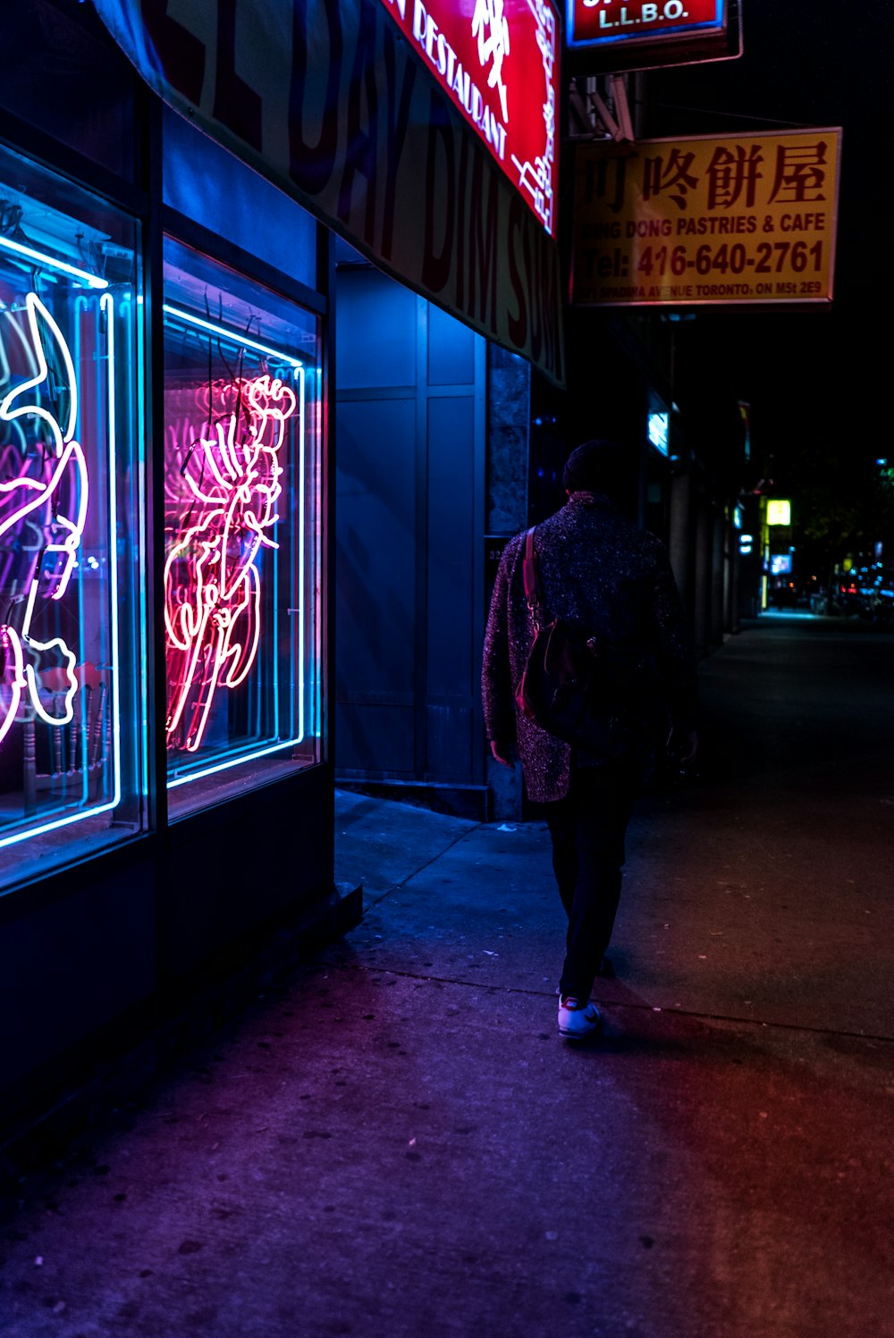 Hombre caminando al lado de una tienda iluminada con luces de neón tomada por la noche
