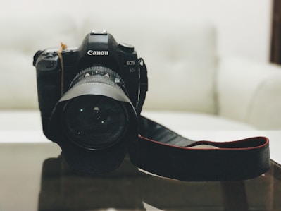 Close-up of a sleek black DSLR camera with a wide lens on a wooden table.