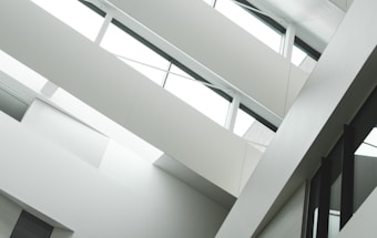 A modern interior with angular architecture, characterized by multiple levels and large windows. The design emphasizes clean lines and a minimalistic aesthetic.