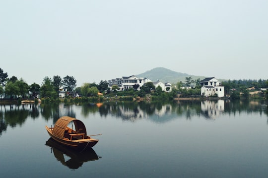 brown wooden boat on body of water overlooking houses by the shore at daytime in Nanjing China
