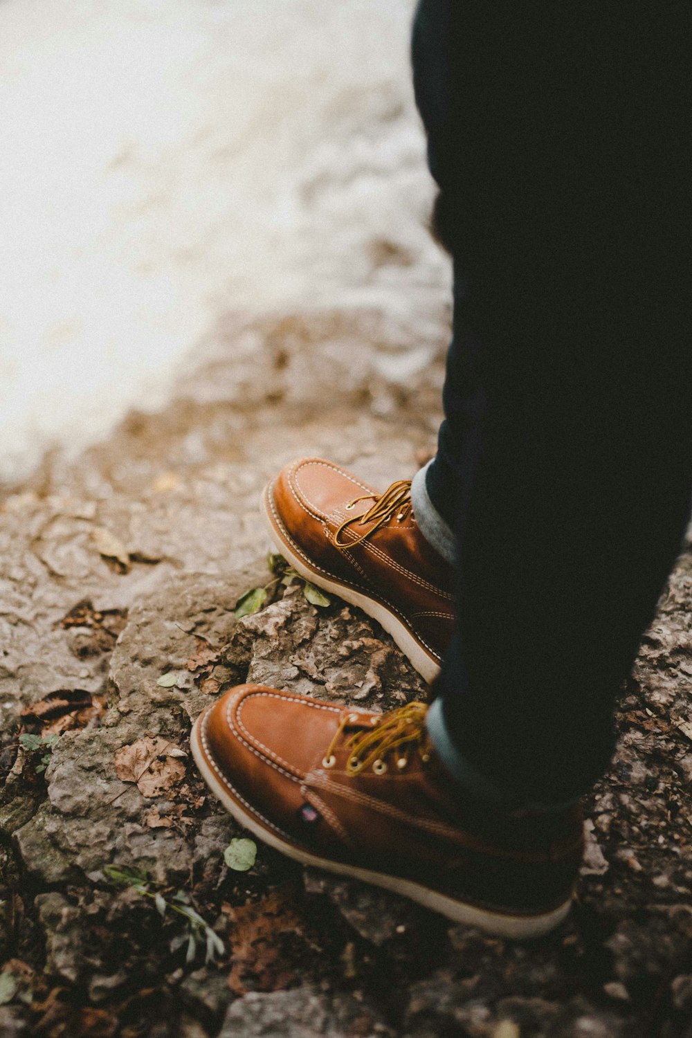 Photographie sélective de mise au point d’une personne portant des chaussures à lacets brunes debout sur un rocher