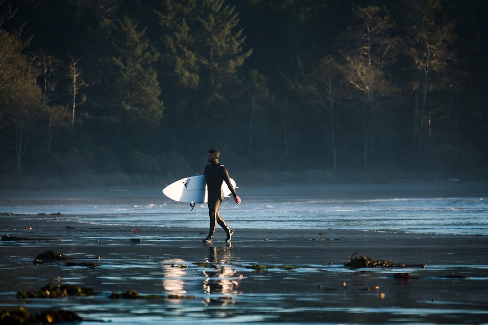 man carrying his white surfboard walking on seashore