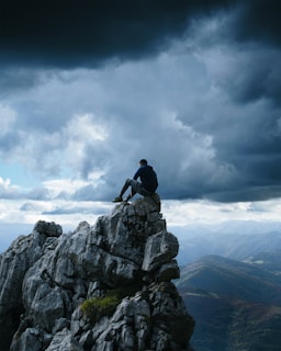 man wearing black pullover hoodie sitting on the high-top rock