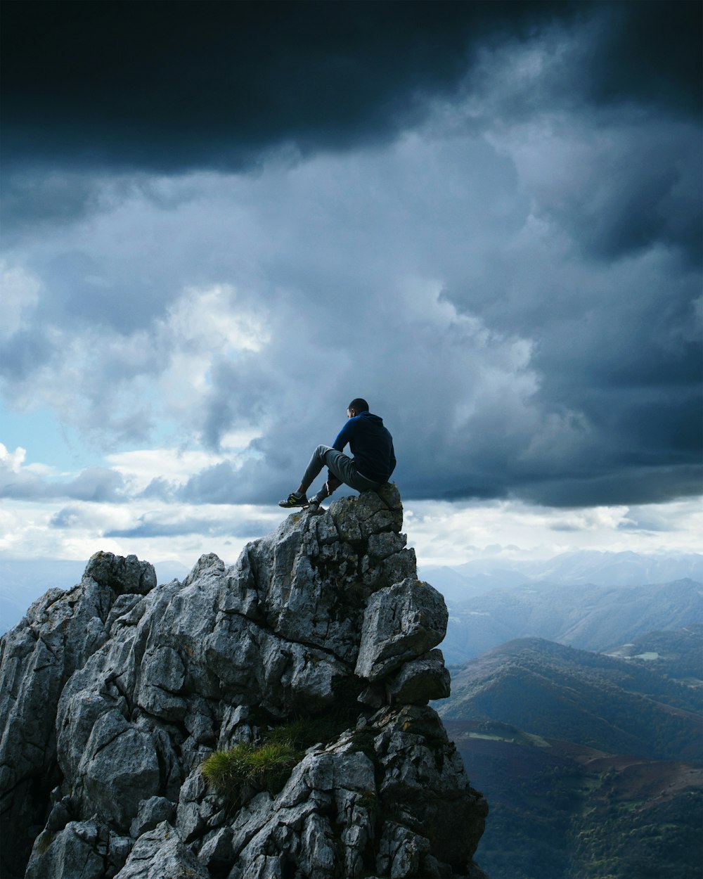 Mann in schwarzem Pullover-Kapuzenpullover sitzt auf dem High-Top-Felsen