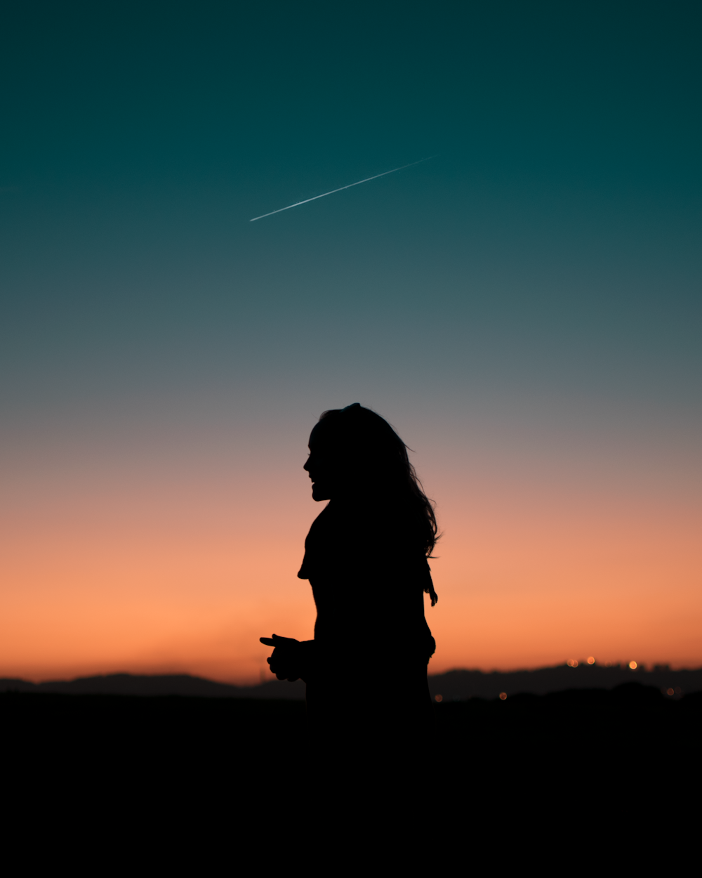 silhouette di donna in piedi sotto il cielo blu durante l'ora d'oro