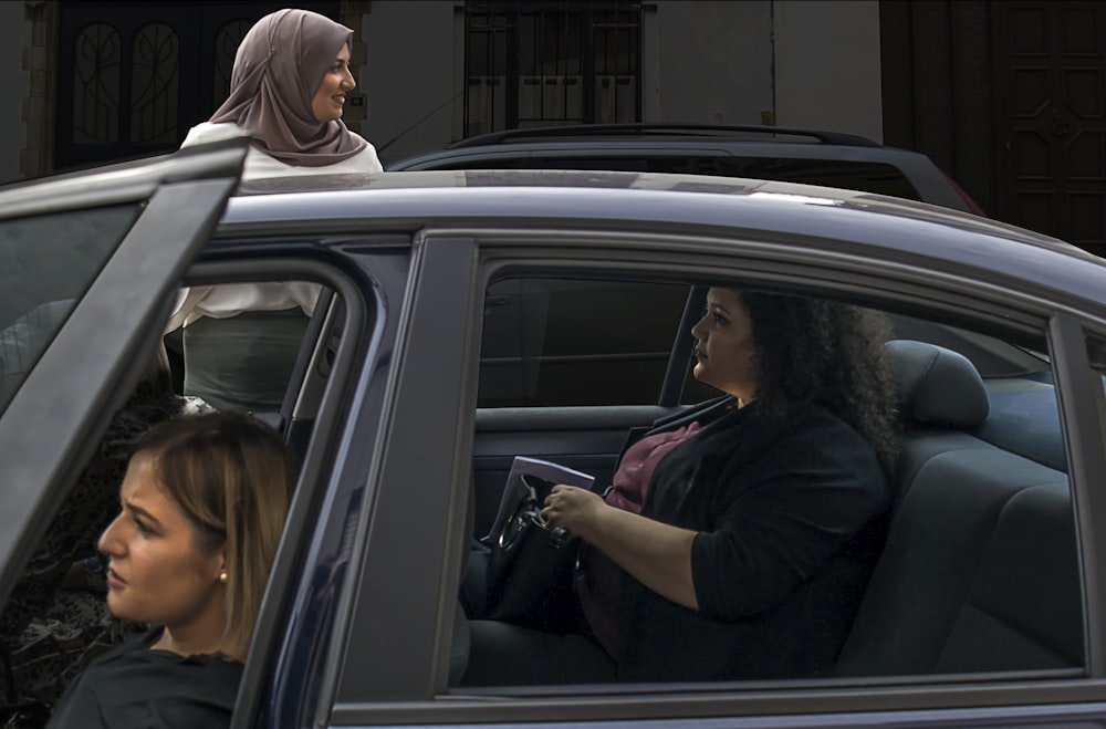 duas mulheres dentro do veículo ao lado de mulher do lado de fora usando lenço de hijab marrom durante o dia