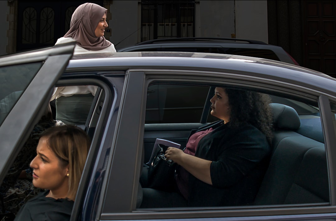 two woman inside vehicle beside woman on the outside wearing brown hijab headscarf during daytime