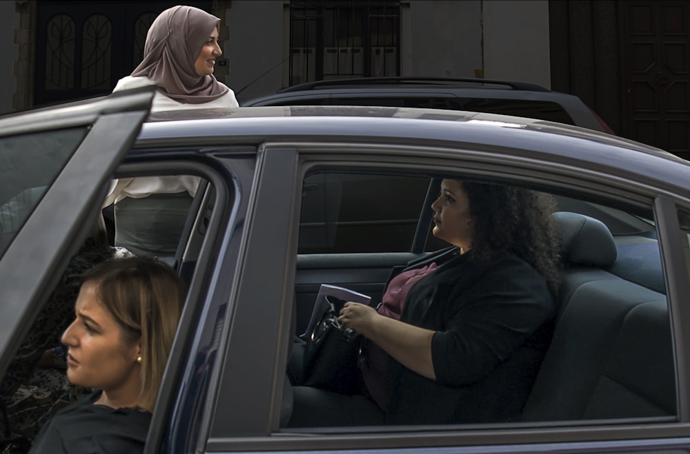 two woman inside vehicle beside woman on the outside wearing brown hijab headscarf during daytime