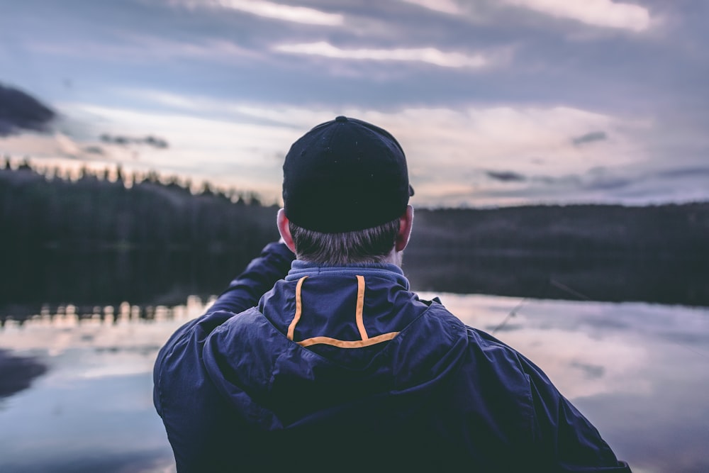 man wearing hoodie facing body of water