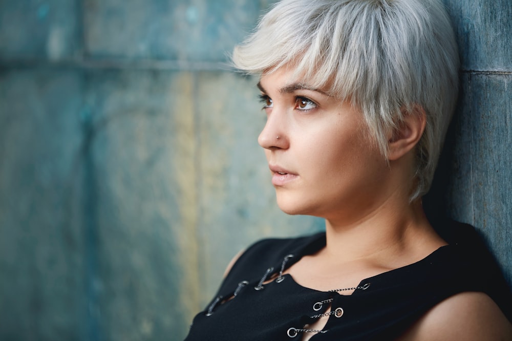 fotografia ravvicinata di donna che indossa un top nero senza maniche appoggiato al muro di cemento grigio