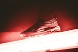 A sneaker placed on top of a fluorescent light, illuminated with a red and pink hue. The sneaker has a sleek design, featuring an air sole and a textured upper.