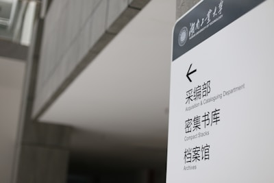 A sign in a modern building displays text in both English and Chinese. It provides directions to the Acquisition & Cataloguing Department, Compact Stacks, and Archives. The setting appears to be a university or a similar institutional environment with a sleek, minimalistic design.