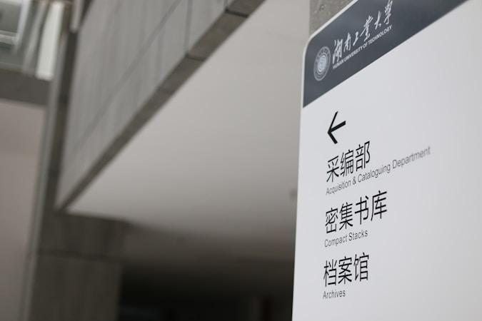 A sign in a modern building displays text in both English and Chinese. It provides directions to the Acquisition & Cataloguing Department, Compact Stacks, and Archives. The setting appears to be a university or a similar institutional environment with a sleek, minimalistic design.