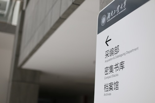 A sign in a modern building displays text in both English and Chinese. It provides directions to the Acquisition & Cataloguing Department, Compact Stacks, and Archives. The setting appears to be a university or a similar institutional environment with a sleek, minimalistic design.
