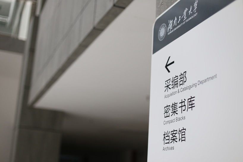 A sign in a modern building displays text in both English and Chinese. It provides directions to the Acquisition & Cataloguing Department, Compact Stacks, and Archives. The setting appears to be a university or a similar institutional environment with a sleek, minimalistic design.